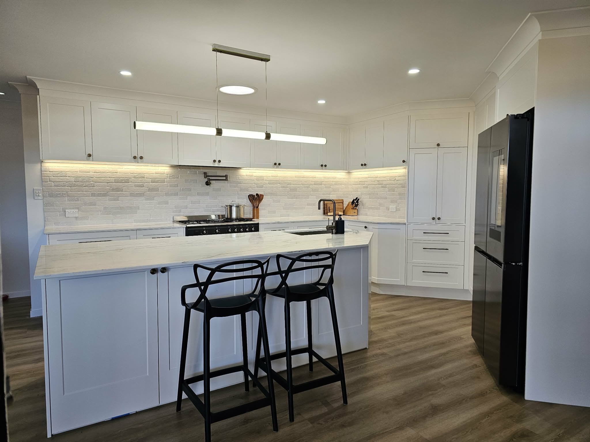Custom white Shaker kitchen cabinetry in Albany Creek, Brisbane, with a stone island breakfast bar, pendant lighting and full-height storage.
